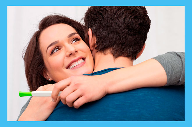 радостная женщина с тестом на беременность обнимает мужчину