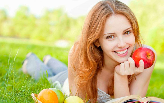 счастливая и здоровая девушка лежит на траве и ест фрукты