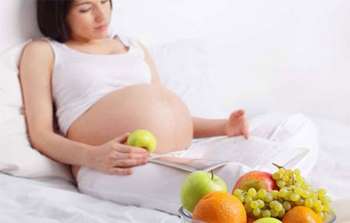 Беременная женщина читает журнал и ест яблоко