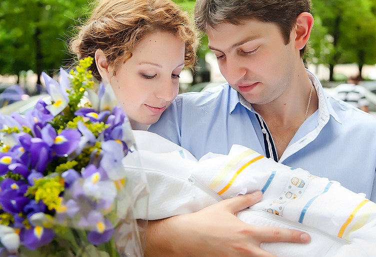 выписка из роддома летом: мама и папа с новорожденным на руках