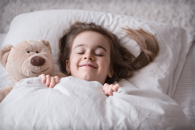 Cute-little-girl-sleeps-sweetly-in-a-white-cozy-bed-with-a-soft-bear-toy-the-concept-of-children-s-r